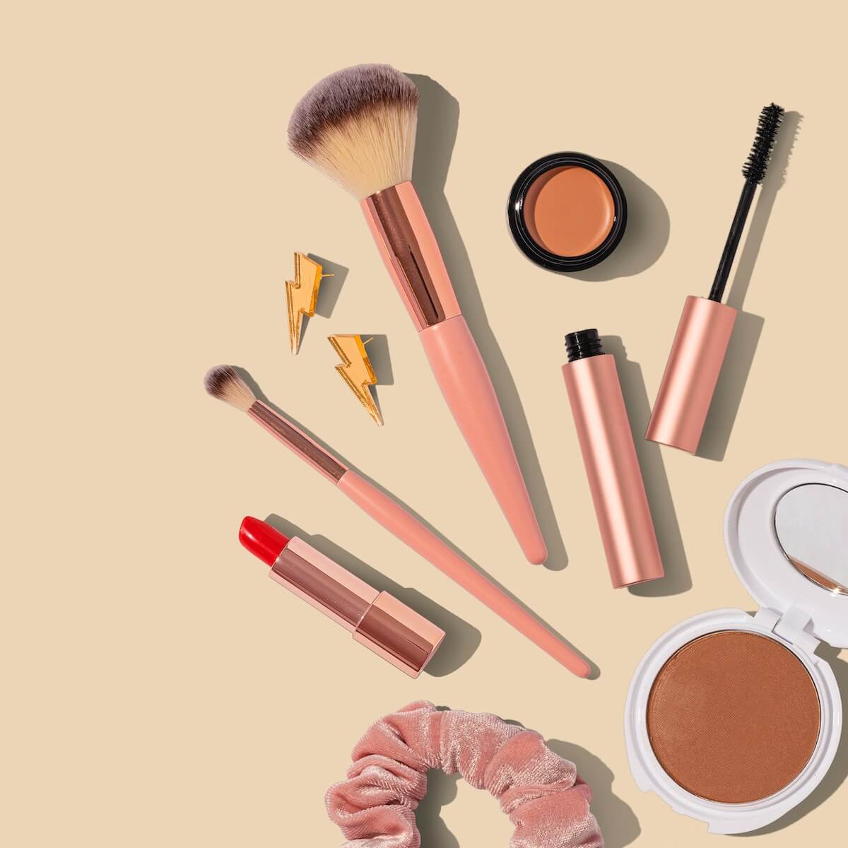 Kwasten, lippenstift en poeder op een zandkleurige ondergrond